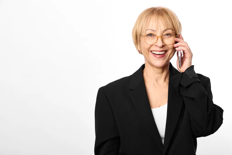 Woman smiling with glasses holding phone near ear, studio portrait on white background, professional communication concept, friendly business mood, bright day
