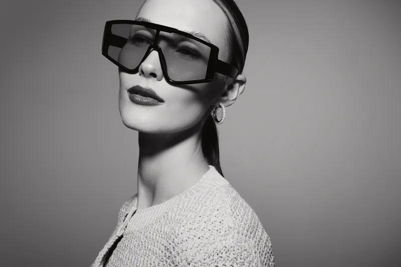 Portrait of a fair skinned white woman wearing oversized sunglasses and textured sweater against plain background. Concept of modern fashion and style.