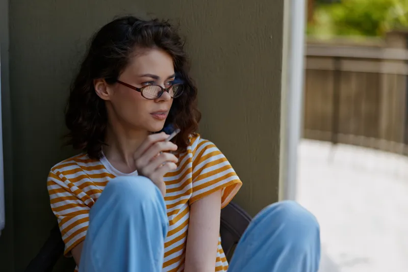 Woman lifestyle at home sits beside a wall in a casual striped shirt and blue pants, thoughtful pose, calm mood, indoor setting, intimate candid moment, serene everyday scene