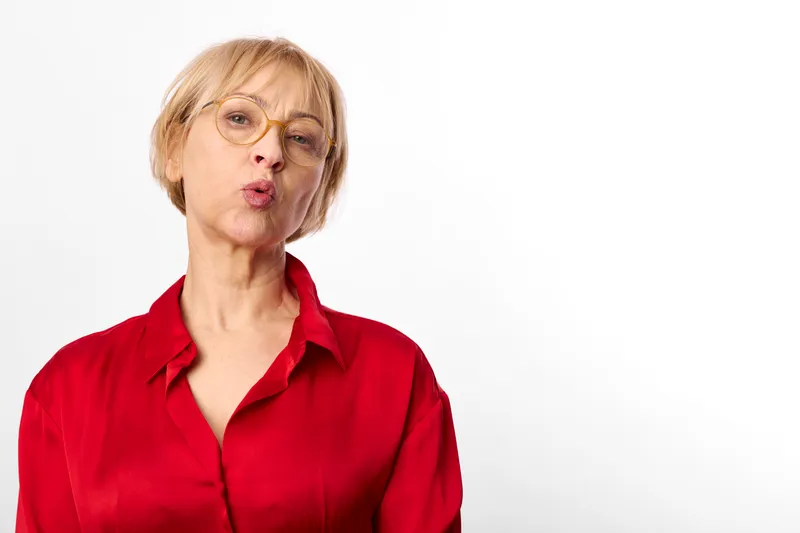 Senior blonde woman in red shirt and glasses, studio portrait, isolated on white background, neutral expression, looking at camera, copy space, calmly