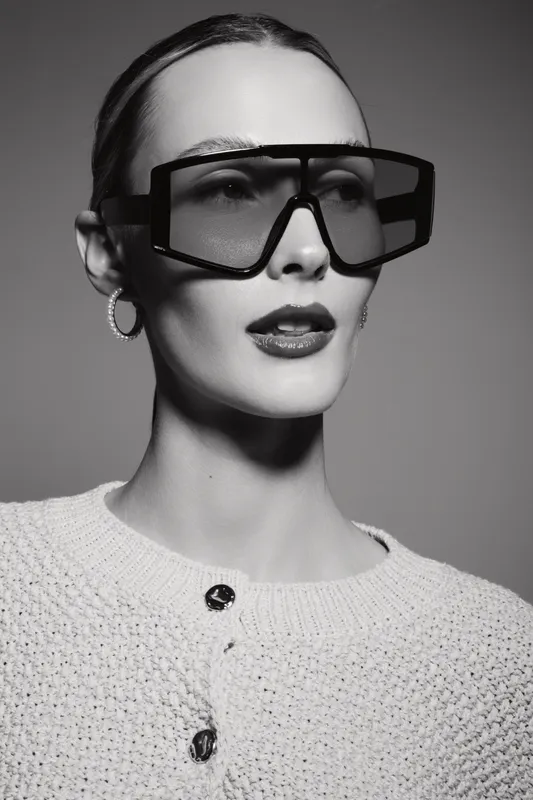 Stylish caucasian woman with pale skin wearing large black sunglasses and knitted sweater in studio. Fashion portrait with neutral background.