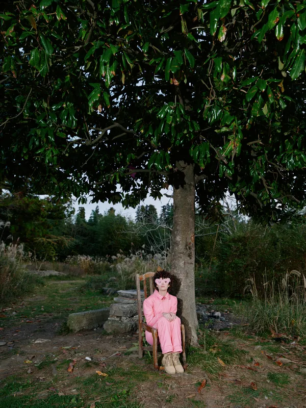Woman sitting under a tree in a pink outfit on a chair outdoors, a tranquil portrait in a garden setting with calm natural light and gentle shade for serene mood