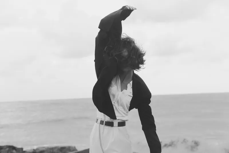 Figure, freedom, motion, silhouette, beach, wind, outfit, raised arm, monochrome, moody, dynamic, cinematic, outdoor, daylight, emotion, drama, movement, shadows, horizon, sea, clouds, style,