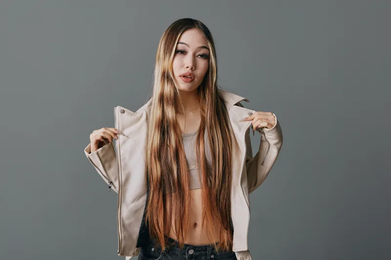 Young woman with long hair wearing casual jacket and crop top posing in studio against plain background for fashion and style portrait photography session.