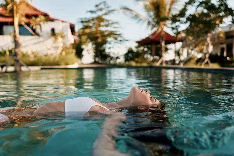 Relaxing woman floats in a clear pool under bright sunshine, enjoying leisure and vacation mood in a sunny resort setting with calm water and tranquil scene