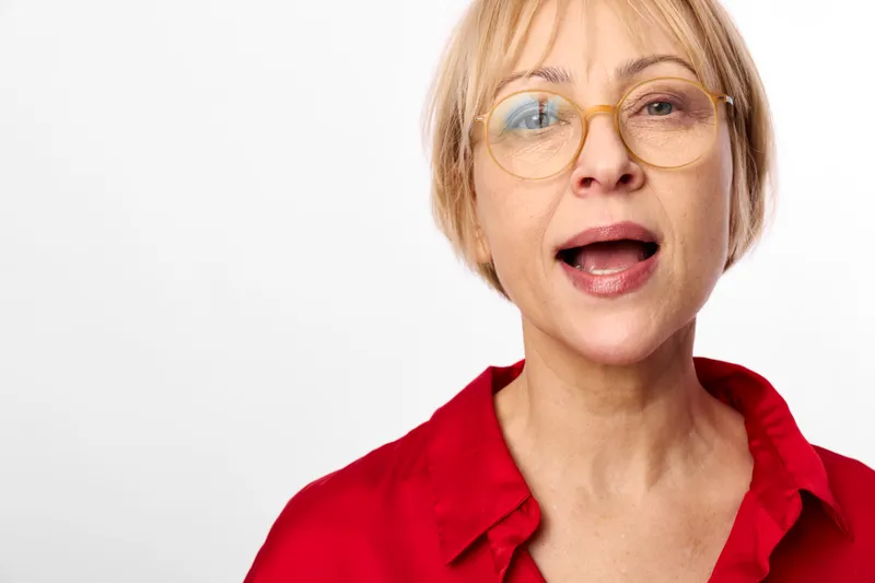Woman with glasses closeup portrait, surprised expression, open mouth, red shirt, studio lighting, neutral white background, soft focus, copyspace