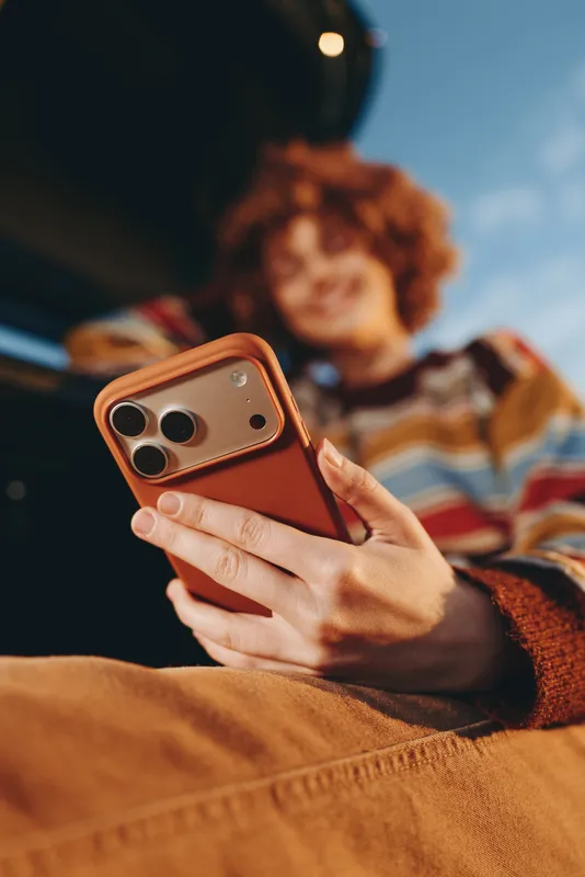 Woman holding smartphone on couch at home, casual lifestyle communication, technology indoors, hands and screen closeup, curly hair girl blurred, cozy leisure moment