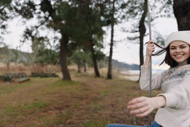 Girl on a swing in a park enjoying outdoor moments, smiling in a casual outfit, trees in background, serene nature scene capturing carefree joy and fresh air.