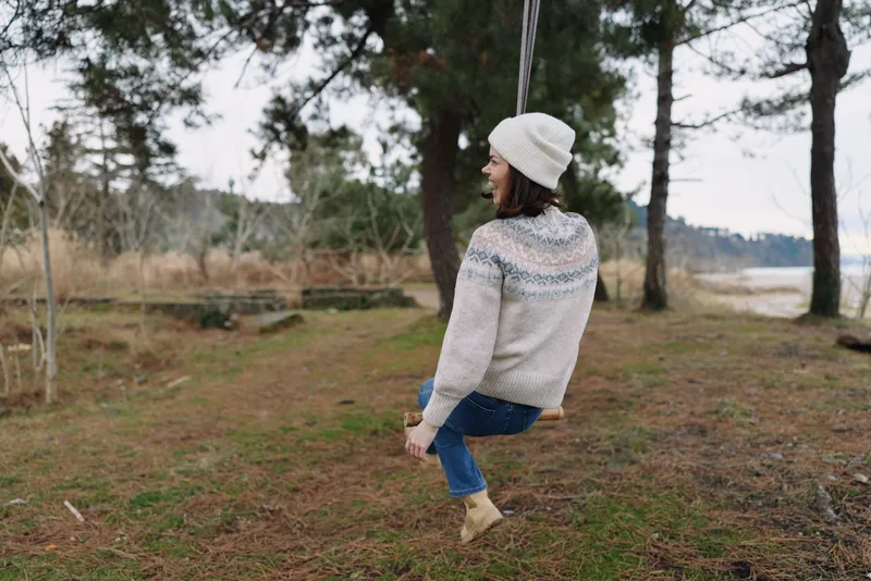 Outdoor swing in a peaceful park, a woman in a knit sweater and hat, enjoying calm nature, casual relaxation and a playful moment in winter scenery.