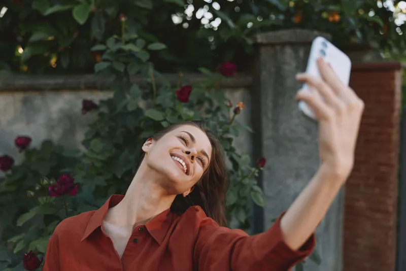 Selfie smiling woman in a red shirt takes a bright outdoor selfie, capturing a candid moment of modern woman lifestyle, confidence, creativity, and everyday joy today
