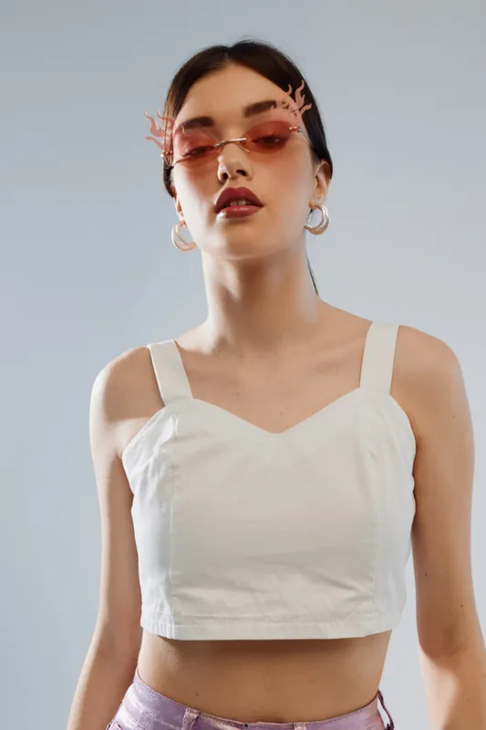 Young woman in a white top and pink sunglasses poses confidently against a grey background. Concept of beauty, fashion, and modern style with minimalistic accessories.