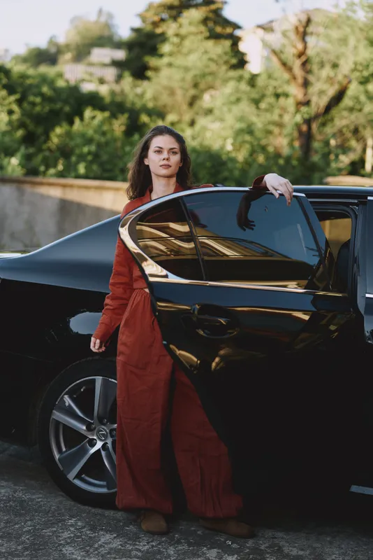 Woman lifestyle fashion car outdoors dress red confidence glamour stepping from a sleek vehicle in a calm urban setting with warm daylight and a relaxed mood