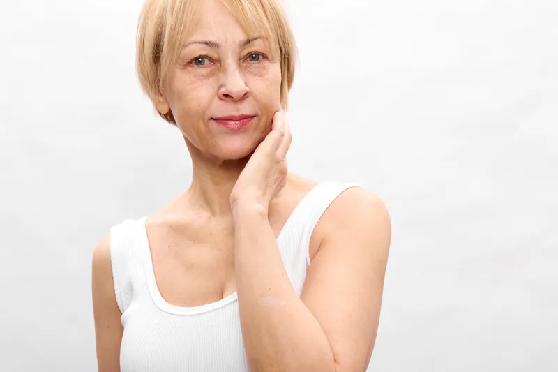 Thoughtful senior woman portrait, hand on chin, face centered on white studio background, calm expression, subtle smile, closeup for reflection, aging and wellness concept