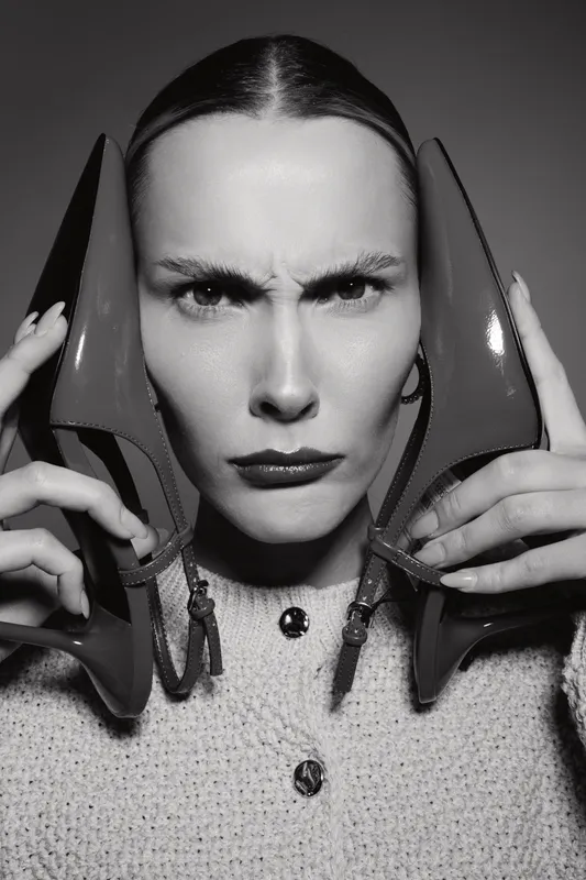 Serious Caucasian woman with fair skin holds red high heels near face with intense expression in studio. Concept of fashion, emotion, and beauty portrait.