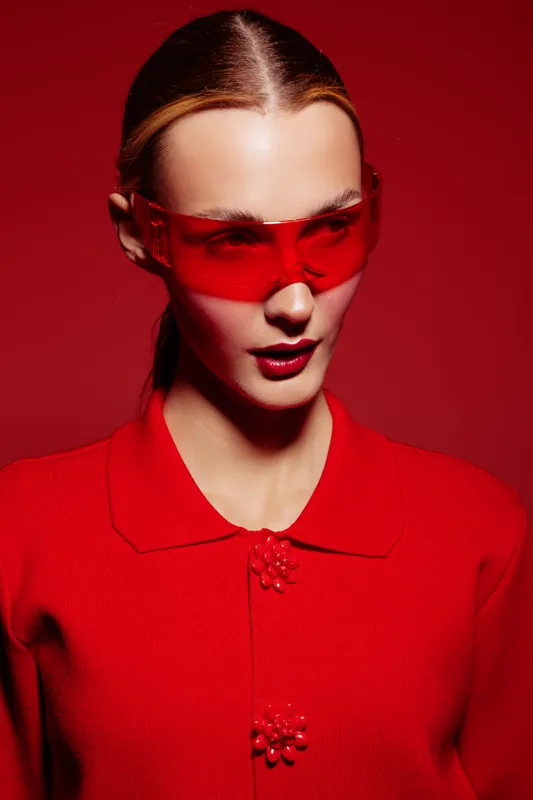 Fashion model in red outfit and red sunglasses poses against red background. Concept of modern style, bold colors, and confident female portrait with sleek hairstyle and makeup.