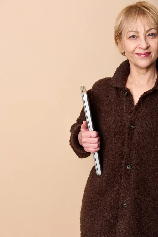 Elderly woman smartphone portrait communication technology smiling studio beige background, friendly headshot, holding mobile device, soft light, calm confidence, everyday digital connection