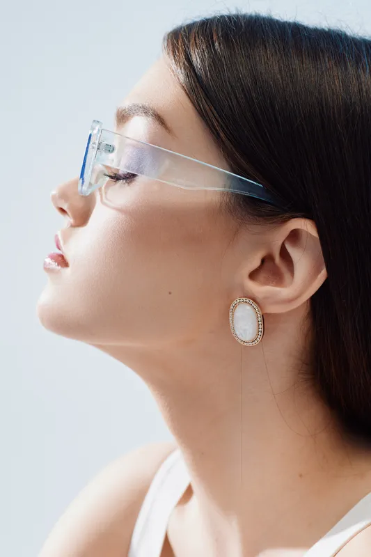 Profile of a young woman wearing transparent glasses and elegant earrings. She has smooth skin and dark hair pulled back. Concept of beauty, fashion, and modern style.