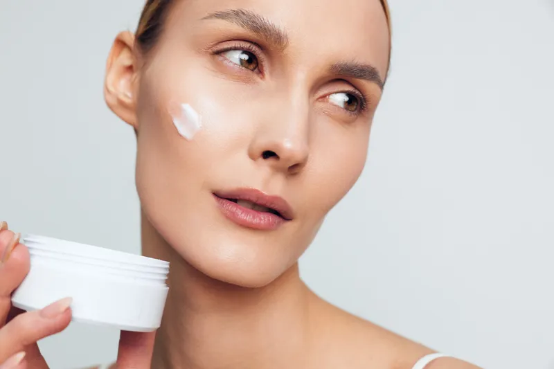 Young woman applying cream on face close up, natural skin care routine, soft light, fresh look, smooth complexion, beauty treatment, healthy lifestyle concept