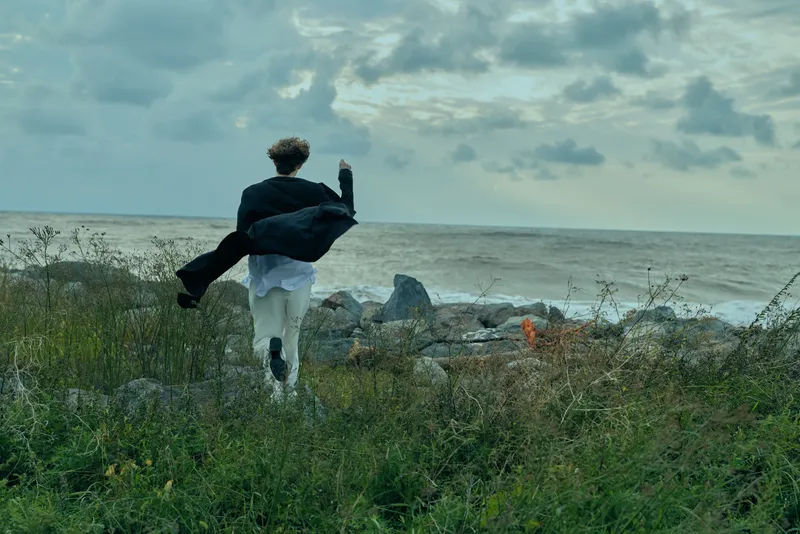 Man in a suit runs along a seaside shoreline, escaping into wind and movement, capturing dynamic energy against a dramatic coastal landscape