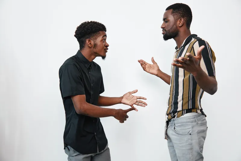Two black men with dark skin having a serious conversation in casual clothes on white background. African ethnicity, communication, discussion, disagreement, standing indoors.