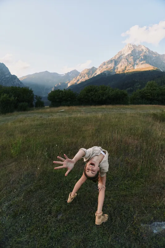Young woman in a sunlit meadow reaches toward the camera with a playful pose as a gentle breeze rustles grasses around her, creating a sense of freedom.