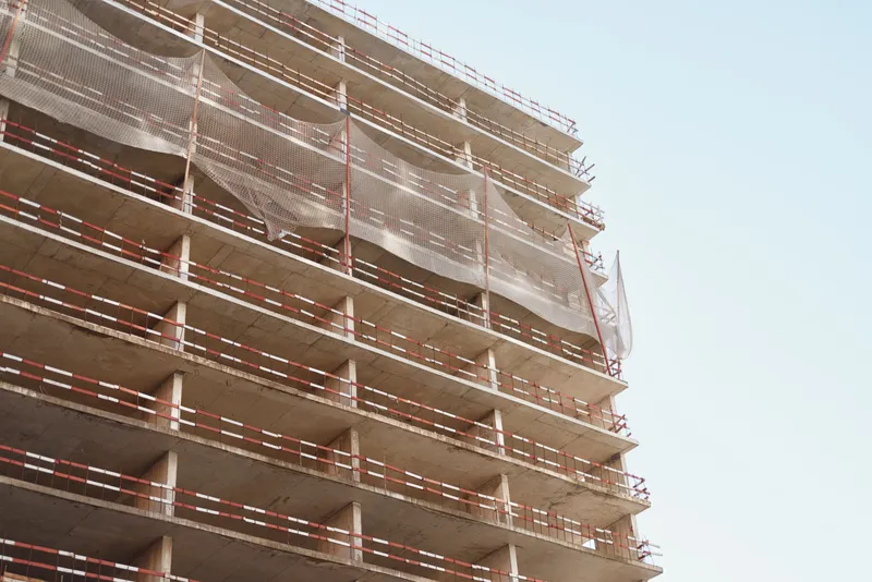 Construction workers wearing safety helmets and vests work on the scaffolding of a multi-story building under clear sky during daytime.