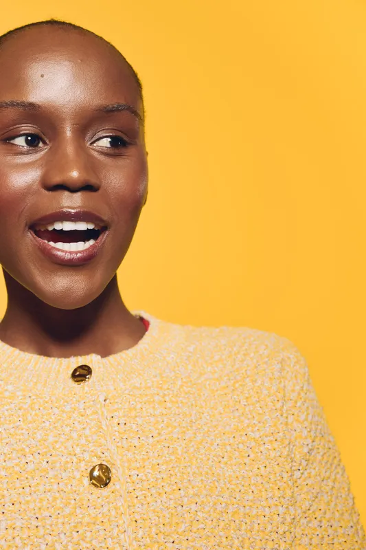 Closeup portrait of a smiling black woman with dark skin wearing a yellow sweater against a bright yellow background. Concept for beauty, fashion, and positive emotions.