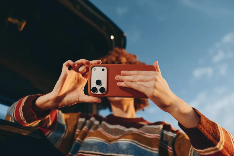 Woman lifestyle selfie portrait, hands hold smartphone to photograph, striped sweater and curly hair visible, outdoors in bright sky, close up casual travel mood, modern everyday communication