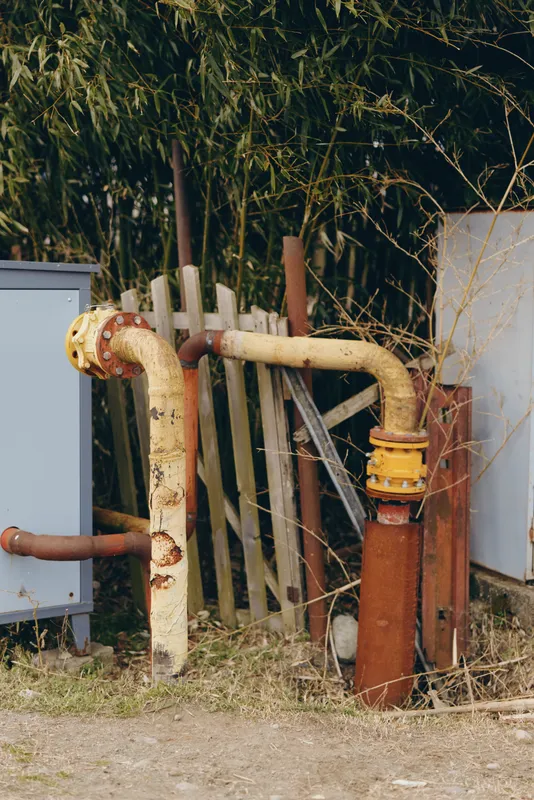 Rust water pump and pipe valve in an outdoor rural yard, maintenance lifestyle for home plumbing repair, weathered metal and dry grass, aged equipment in daylight