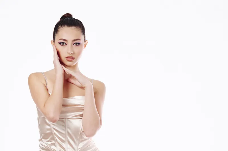 Beautiful young woman with flawless skin and makeup poses with one hand on her face and the other near her neck in elegant studio lighting. Beauty creative fashion concept.