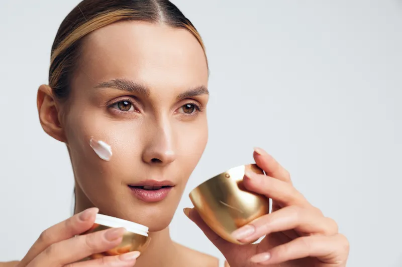 Closeup of woman applying face cream, skincare routine, smooth skin texture, natural beauty, focused expression, soft lighting, clean background, cosmetic jar in hand