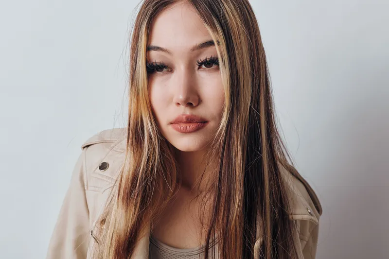 Young woman with long straight hair and neutral expression wearing trench coat on plain background, portrait and fashion style with natural makeup and hairstyle.