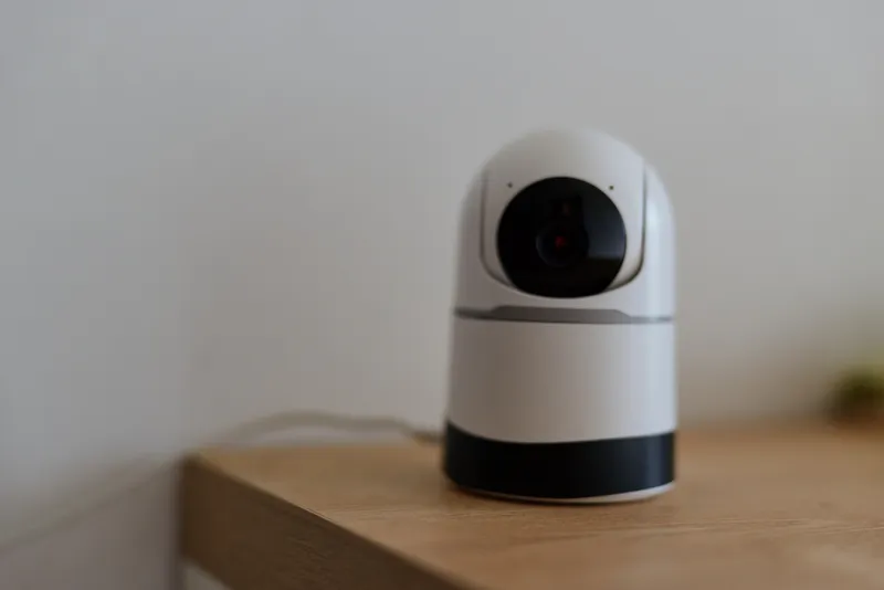 A compact indoor surveillance camera sits on a wooden table, quietly monitoring the room and providing a sense of safety in a modern home environment.