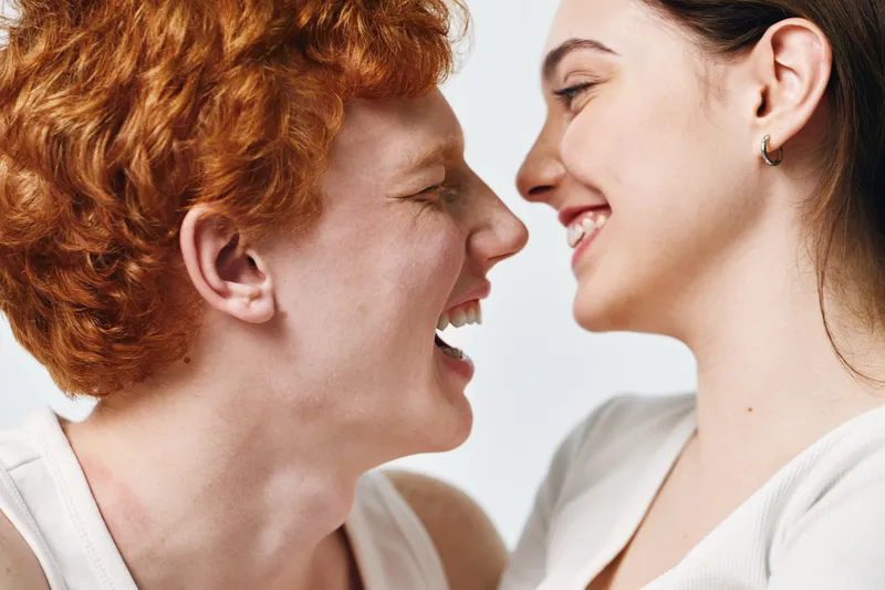 Young couple laughing and smiling closely, enjoying happy moment together. Man and woman face to face with joy and affection on light background.