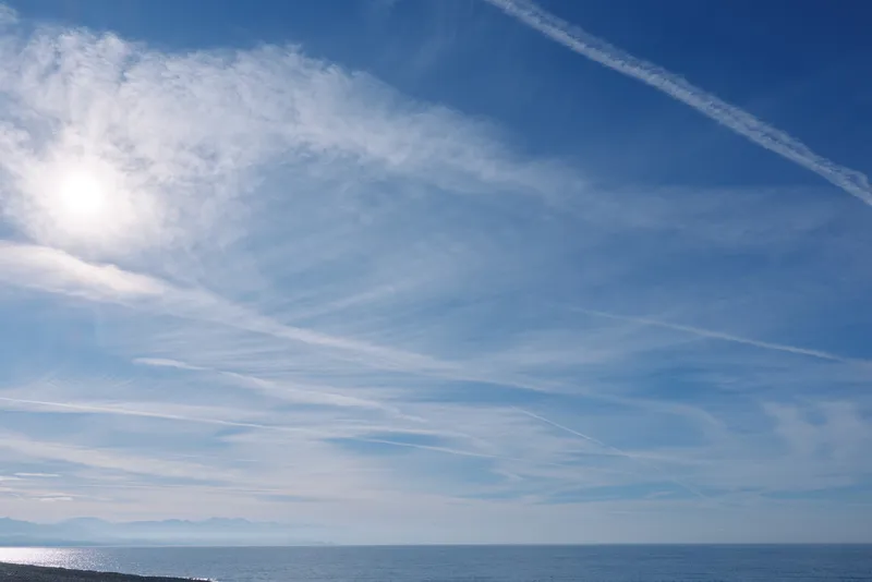 Clear sky over a calm sea with a bright sun and wispy clouds along the horizon, creating a tranquil coastal landscape ideal for nature and travel themes.