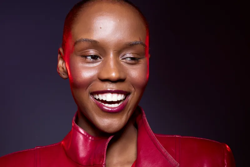 Close-up of a smiling black African woman with dark skin wearing a red leather jacket. Studio portrait with soft lighting on a dark background. Concept of fashion, beauty, and confidence.