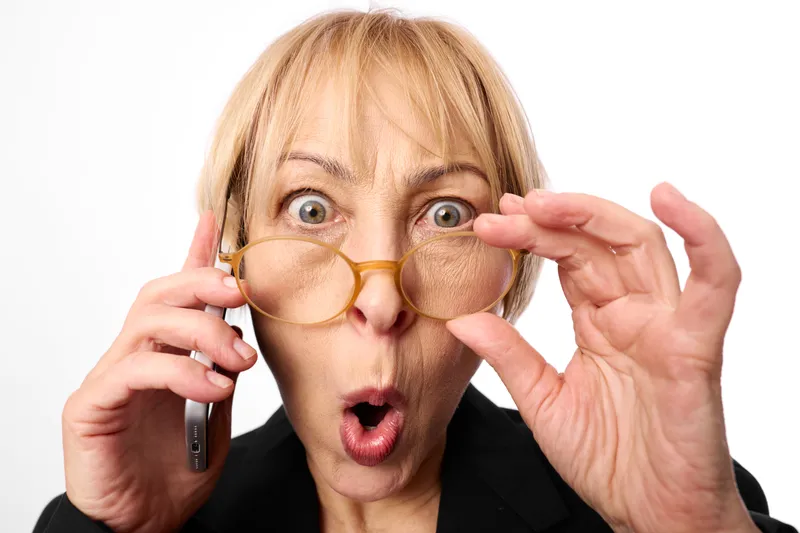 Elderly woman studio portrait on white background, surprised expression, holding novelty eyeglasses and glasses, phone call gesture, mouth open, looking at camera, soft light