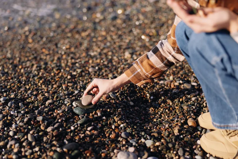 Hand reaching for a rock on a pebbled beach, capturing outdoor exploration and casual nature activity in soft sunlight and calm seaside ambiance.