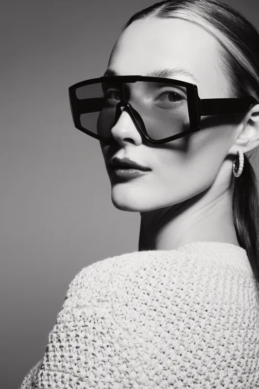 Portrait of a young white woman wearing large futuristic glasses and a textured sweater in black and white studio lighting.
