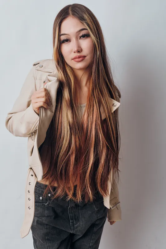Young woman with long straight hair wearing casual clothes stands against light background looking at camera with confident expression in fashion portrait studio shot.