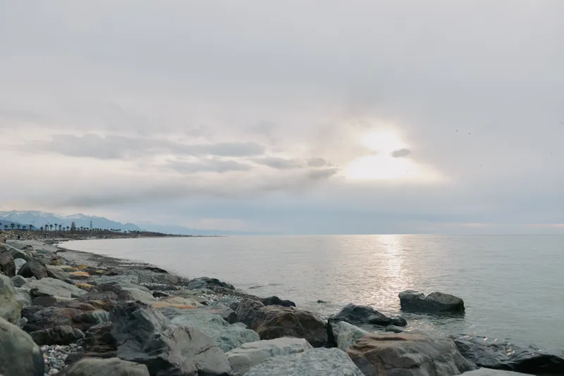 Rocky coastline with calm sea under cloudy sky during sunset. Soft light reflects on water surface, creating a peaceful and serene atmosphere by the shore. Concept of nature and tranquility.