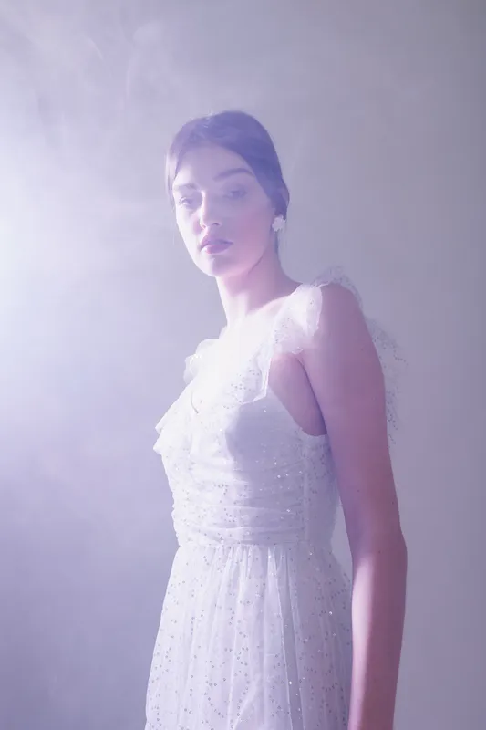 Woman beauty fashion wearing a white elegant dress stands in soft misty light. Her calm expression and delicate makeup create a dreamy atmosphere. Studio shot with soft focus.
