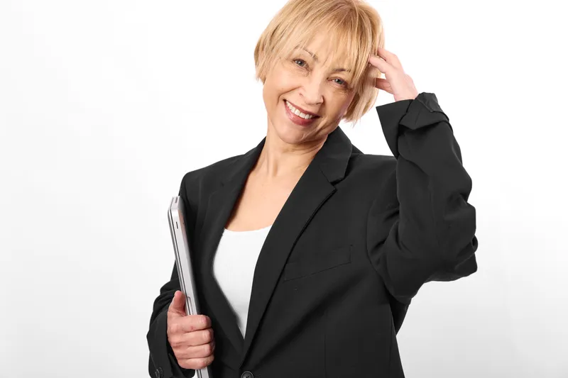 Businesswoman blonde in suit smiling, holding folder with papers, posing portrait on white studio background, hand on hair, professional work style