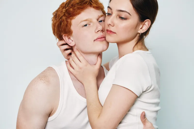 Couple, young man and woman in white clothing embracing and posing on blank background with close connection and intimate expression for love and relationship.