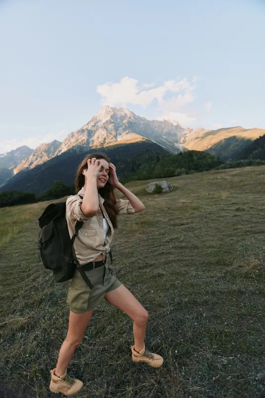 A woman on a mountain hike with a backpack explores rugged terrain, the distant range behind her, conveying adventure and outdoor lifestyle.