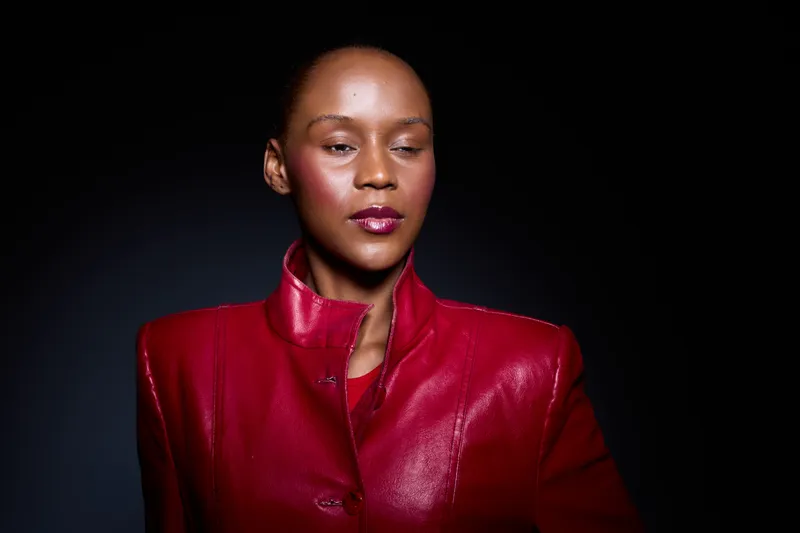 Portrait of a confident black woman with dark skin wearing a red leather jacket, eyes closed, isolated on black background. Concept of fashion, elegance, and empowerment with studio lighting.