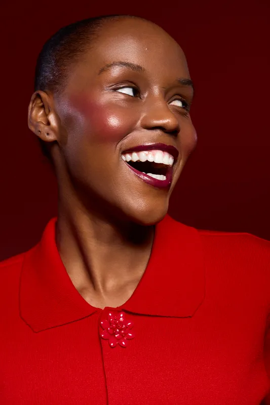 Happy smiling African woman with dark skin wearing red clothing looks sideways. Close-up portrait on red background. Concept of joy, beauty, fashion, and positive mood with vibrant colors.