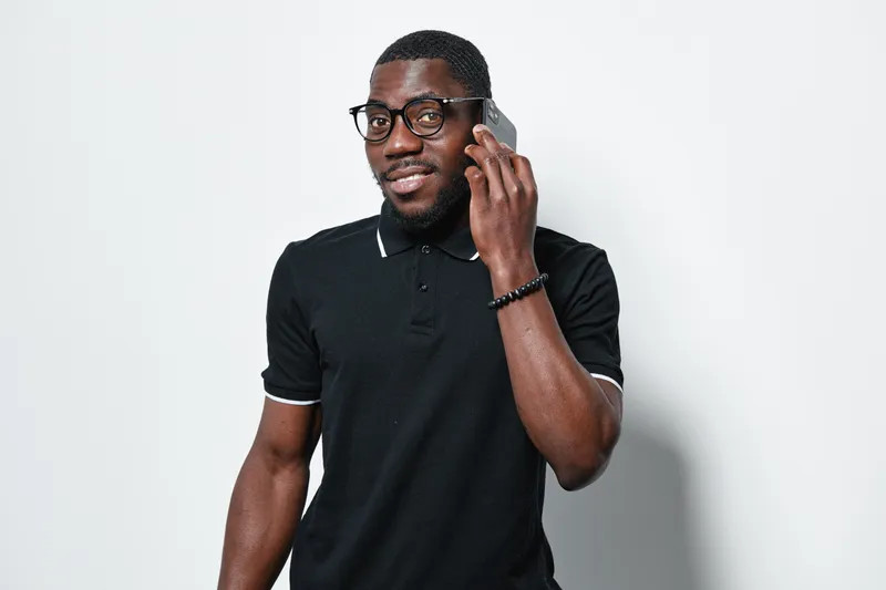 African american man with dark skin and glasses talking on smartphone in casual black polo shirt isolated on white background. Communication, technology and lifestyle concept.