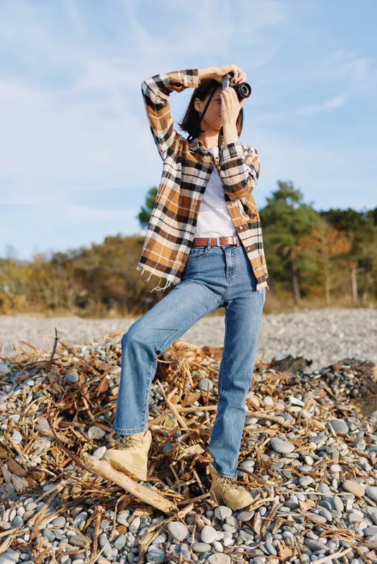 Outdoor fashion, casual wear with plaid shirt and jeans, boots, model posing on a rocky landscape with hands shielding eyes under a bright sky, nature backdrop and relaxed attitude