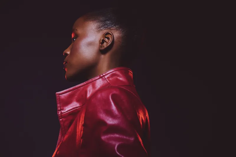 Profile of a black woman with dark skin wearing a red leather jacket against a dark background. Concept of fashion, confidence, and modern style with dramatic lighting.